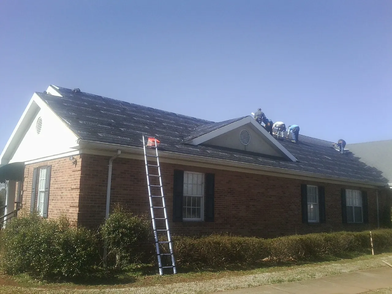 Crew tearing shingles off a brick ranch roof with a ladder set — Metal Roof Repair work by our crew in Crestwood