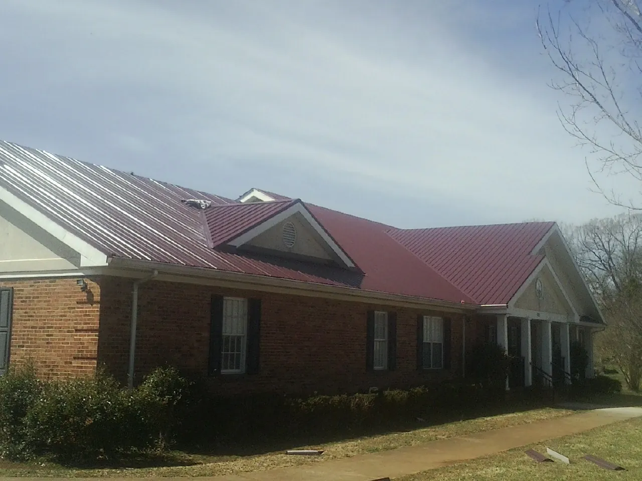 Red metal roof with gabled entries on a long brick building, from a Hail Damage Roof Repair job in Crestwood
