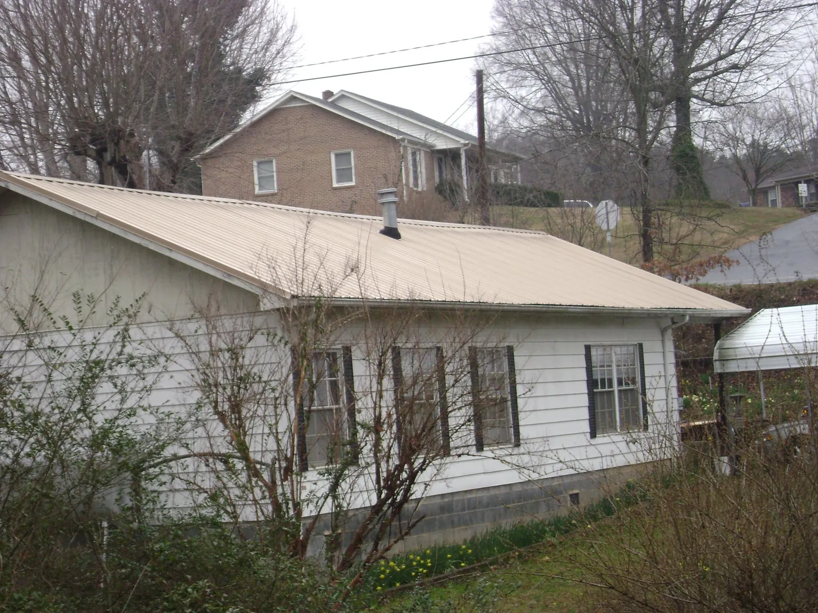 Tan metal roof on a white sided house set into a hillside — Commercial Roofing by Roofing Brothers in Crestwood